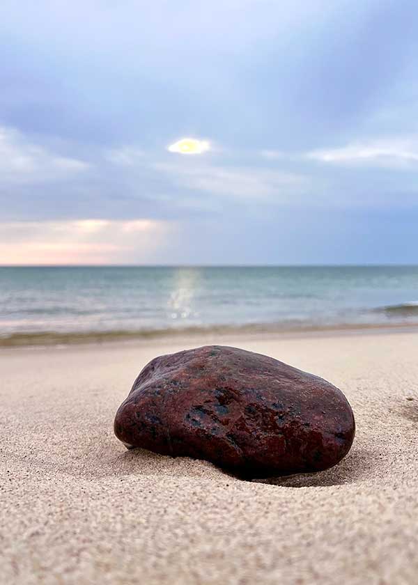 Flot sten ligger på stranden, farver, himmel, sand, vand og solen spiller sammen på smukkeste måde