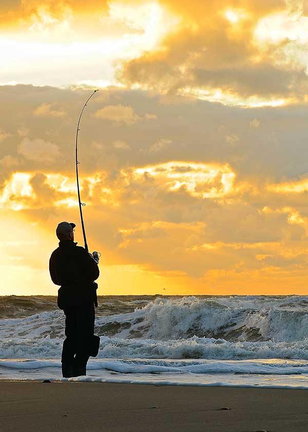 Lystfiskeren er gået igang med aftens fiskeri på kysten, han tegner sig som en silhuet mod den "brændende" himmel