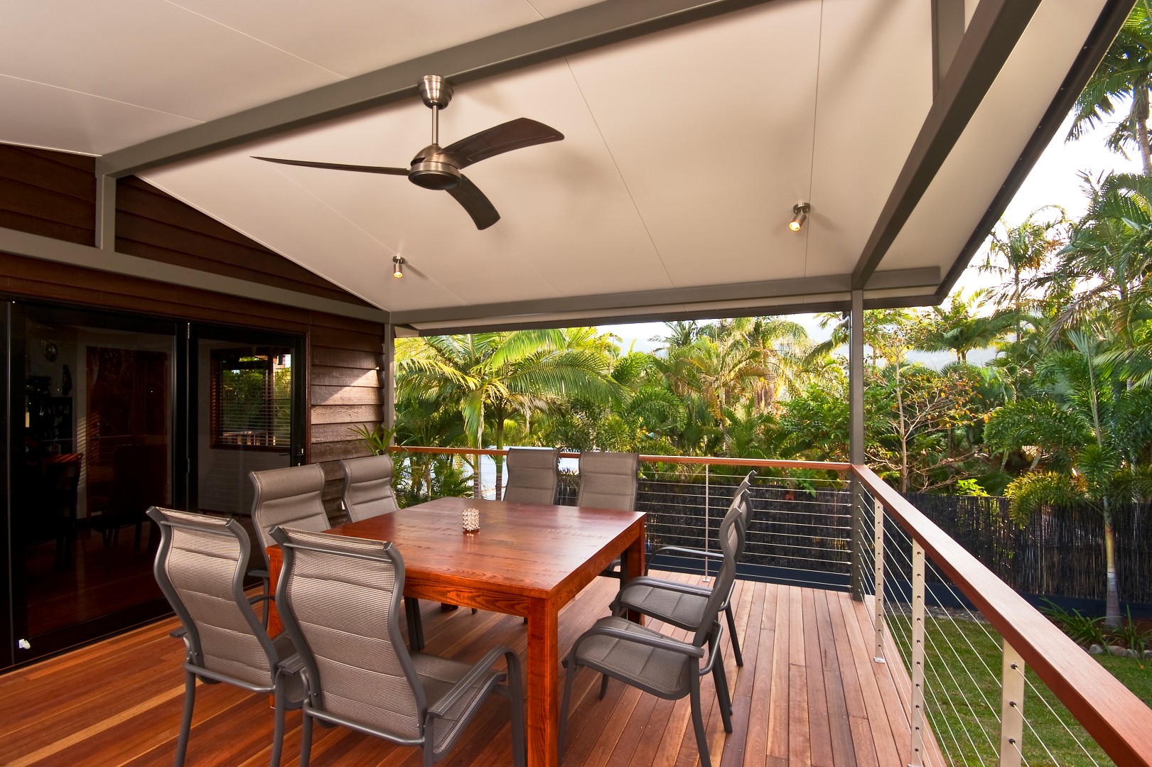 A wooden deck with outdoor furniture and a ceiling fan overlooking lush greenery, typical of Perth patios. Phoenix Patios, Cottages and Granny Flats in Perth
