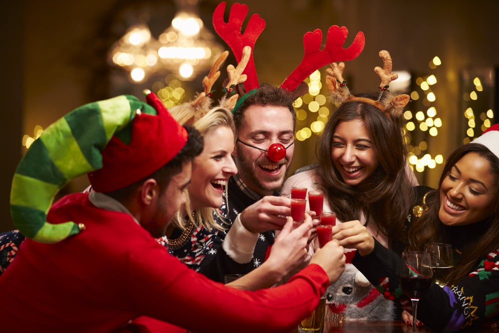 A group of people in ugly sweater christmas hats toasting at an official party.