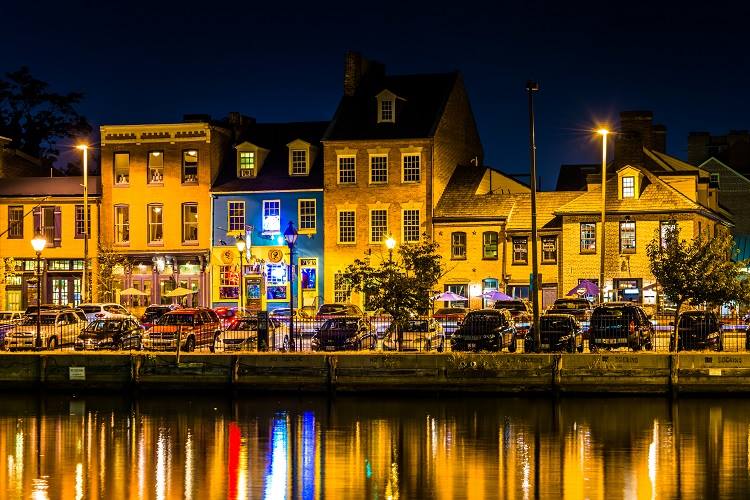 A festive view of Fells Point at night with cars parked by the water.