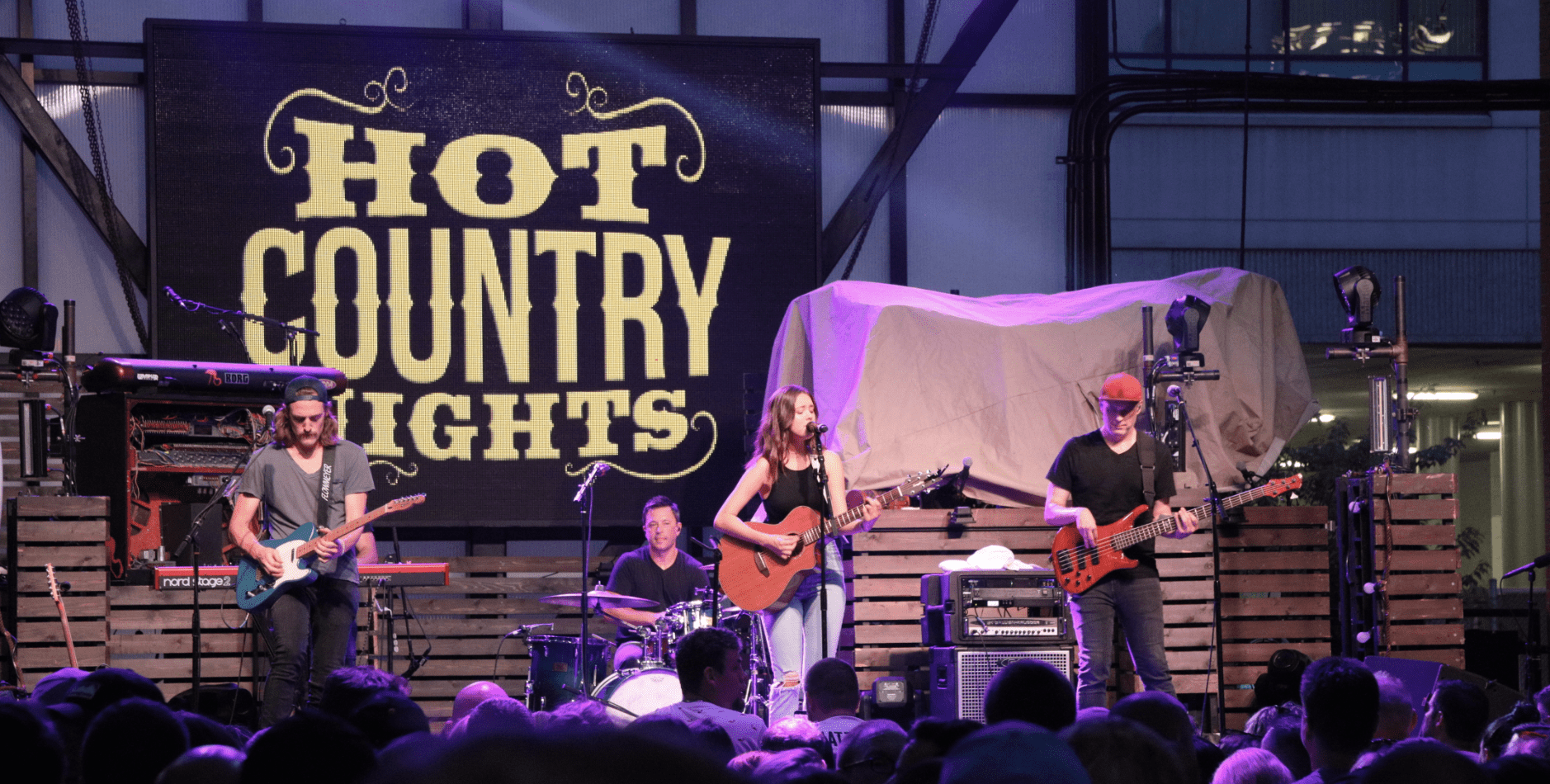 A group of people on stage at a concert with the words hot country nights.