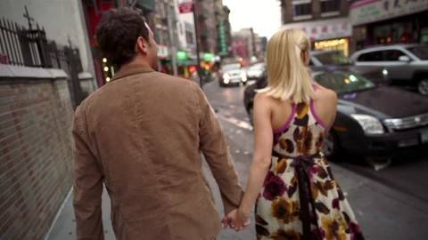 A man and woman walking down a city street holding hands.